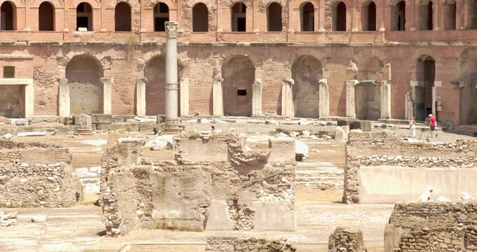 An impressive view of the historic Trajan's Market ruins in Rome, Italy, featuring ancient brick arches, a standing marble column, and layered stone foundations under the bright, warm Italian sunlight