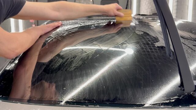 Professional car window tinting process: technician prepares the glass, applies tint film, uses a heat gun to shape it on curved surfaces, and smooths out air bubbles with a squeegee. 