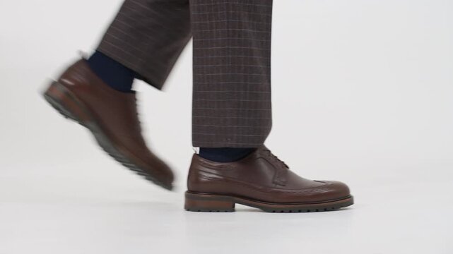 Businessman's legs in brogues and plaid trousers walking on a white background, studio shot