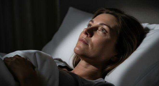 Woman lying awake in bed at night suffering from insomnia. Female experiencing hormonal sleep disturbance or mood change. Anxiety and mental health concept during hormonal cycle shift.
