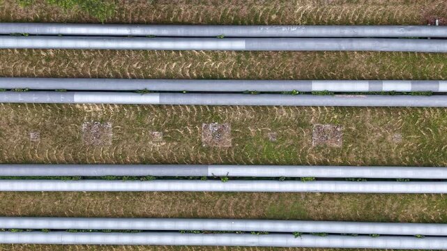 Aerial view of industrial pipes arranged in parallel lines across grassy terrain, showcasing the continuous flow and connection of gas and water infrastructure in an outdoor setting