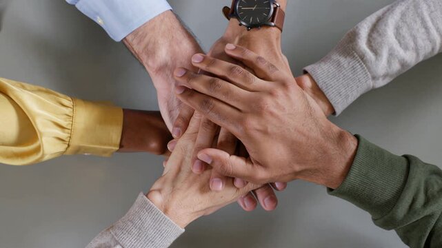 Diverse business team stacking hands on a table, symbolizing teamwork, unity, and successful collaboration in a corporate office setting, a powerful top view gesture