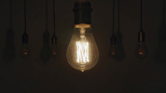 Vintage edison light bulb hanging and glowing in the dark, symbolizing a bright idea, innovation, and creativity, surrounded by other unlit lamps in the background