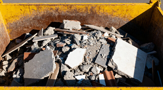 Full yellow skip bin containing renovation waste, bricks, and rubble at outdoor construction site.