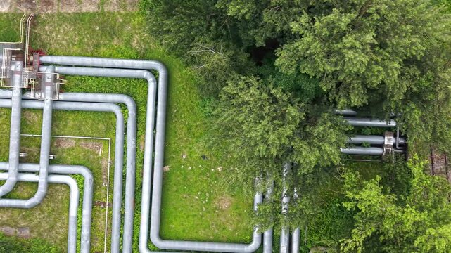 Aerial view of industrial pipes winding through a green urban landscape, showcasing the intricate layout of infrastructure alongside buildings and trees in a city setting