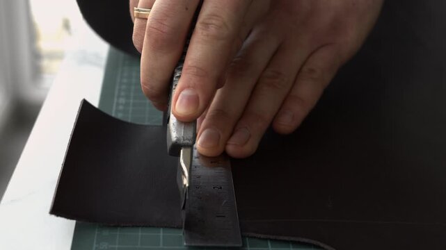 Artisan craftsman cutting genuine leather with a ruler and utility knife in a workshop for handcrafted goods