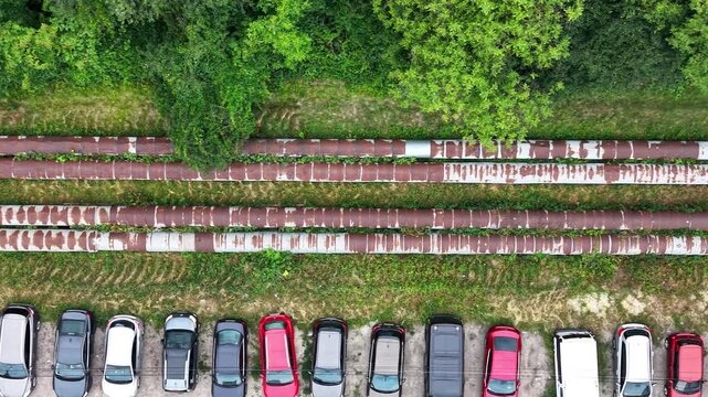 Aerial view of parked vehicles alongside rusty metal pipes and overgrown vegetation, showcasing the gradual transition of the landscape and parking arrangement in a natural setting