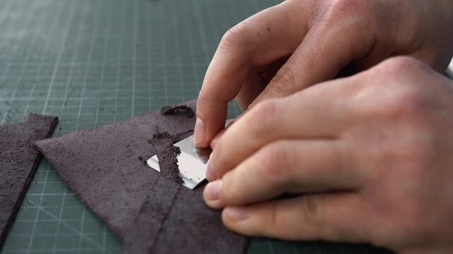 Close-up of artisan's hands skiving leather for crafting a handmade wallet or purse on a cutting mat
