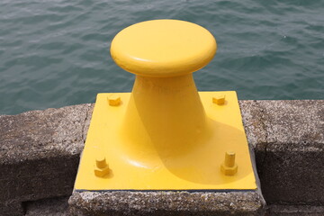 Obraz premium yellow maritime mooring bollard, cast iron or cast steel, anchored directly into concrete quay (close-up, waterfront) 4657