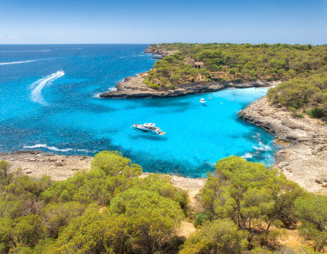 Aerial view of sea in Mallorca, Spain. Luxury yachts, boat anchored in turquoise water cove, rocky coast with green pine trees, sandy beach on sunny summer day. Mediterranean drone landscape. Vacation
