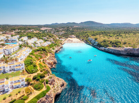 Aerial drone view of sandy beach and sea bay in Mallorca, Balearic islands, Spain. Top view of turquoise water, boats, yachts, resort hotels, green trees, rocky cliffs. Mediterranean landscape. Summer
