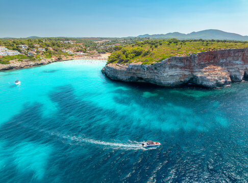 Aerial view of motor boat near resort beach in Mallorca, Spain. Top view of Luxury speedboat cruising in turquoise sea water bay, sandy beach, hotels on high rock cliffs in summer. Drone seascape