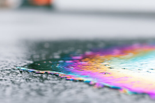 Rainwater puddle oil sheen angled side view of shallow puddle with rainbow surface tension and blurred walkway background