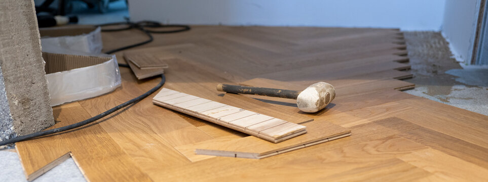 Rubber mallet and engineered oak parquet planks prepared for herringbone floor installation on acoustic underlay during modern home renovation