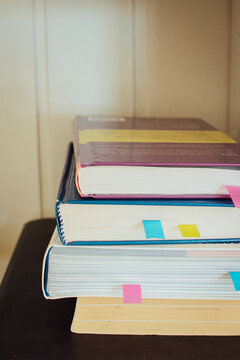 Close-up of a stack of hardcover books with colorful sticky notes and tabs in the pages