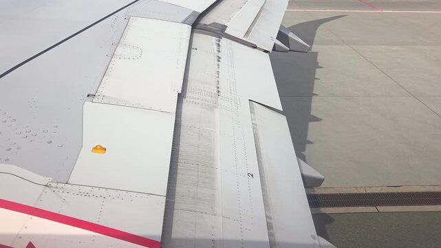 Aircraft wing with extended flaps and slats visible during taxiing on runway, showcasing mechanical components and surface details in a clear sky environment