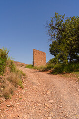 Naklejka premium Wanderlust meets history on a sunbaked gravel path leading to a crumbling medieval stone tower in Valencia Province. Perfect for travel, heritage, and adventure editorial use.