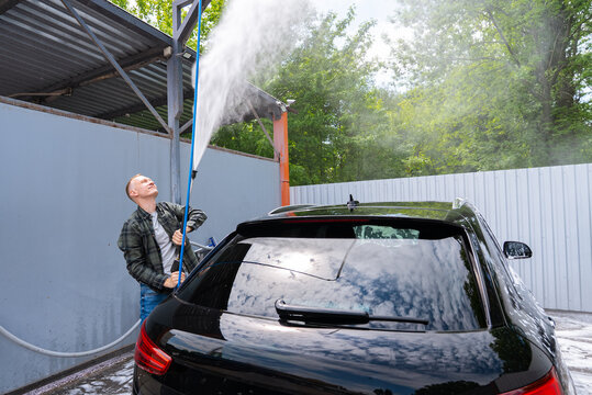 Man washing car at self service car wash with spray wand