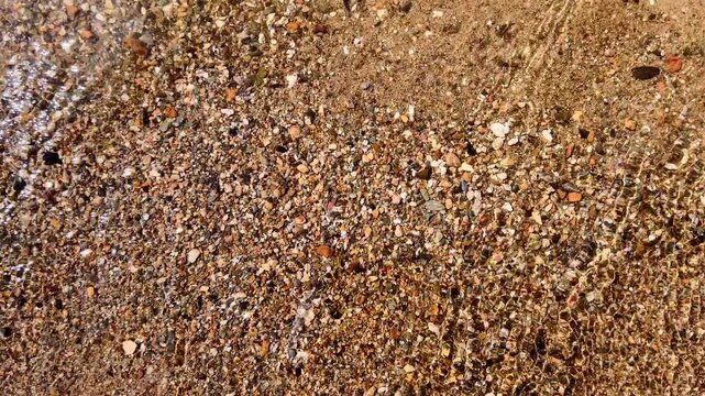 Sandy lakeshore with foamy shallow waves washing over wet pebbled sand creating natural texture