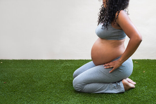 Pregnant woman kneeling on grass, maternity lifestyle pose