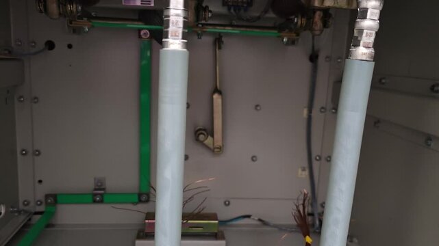Panning right video of three phase underground electrical power cables with crimped metal lugs fully terminated inside a medium voltage switchgear cabinet.