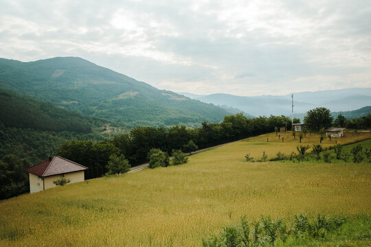 Green mountain valley with rural fields, scattered houses and forest under a cloudy sky. Peaceful countryside, sustainable living and nature tourism.