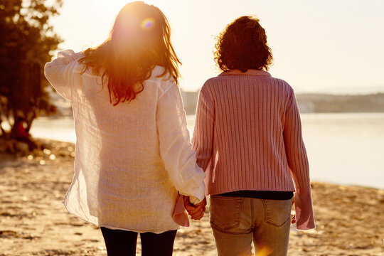 Two friends holding hands at sunset by a quiet beach