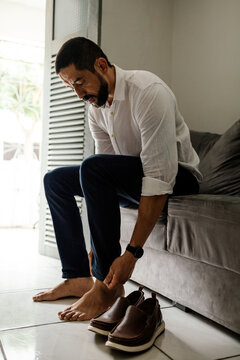 Mature man putting on leather shoes at home while getting ready to leave, capturing an authentic moment of everyday fashion and routine.