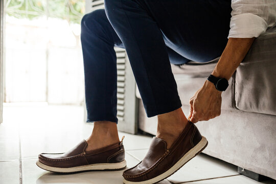 Mature man putting on leather shoes at home while getting ready to leave, capturing an authentic moment of everyday fashion and routine.