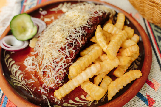 Traditional gourmet pljeskavica served with crispy French fries, grated cheese, fresh onion and cucumber. A hearty Balkan grilled meal presented on a rustic ceramic plate.