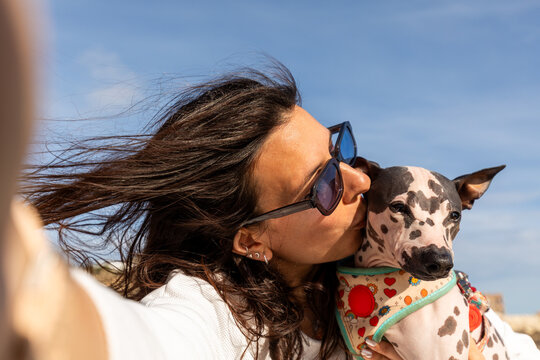 Woman kissing American Hairless Terrier on windy walk
