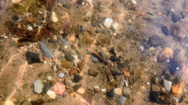 River bottom with pebbles and sand visible through flowing water waves in motion