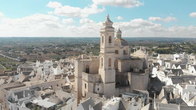 Horizontal 4K drone video of Locorotondo in Puglia, Italy. Aerial view of the historic town center focusing on the ancient San Giorgio Martire church tower and traditional white houses