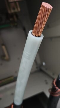 Pan up video of a stripped underground electrical power cable showing exposed copper strands and white insulation prepared for termination inside a switchgear cabinet.
