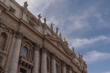 Obraz premium Low-angle view of ornate Baroque church facade with Corinthian columns, roofline statues and decorative pediment against a blue sky