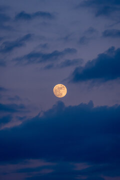 Full moon glowing through dark blue clouds at twilight