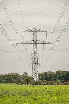 High voltage power line pylon over green rural field
