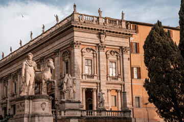 Fototapeta premium Historic ornate stone building facade with classical statues and warm evening light, Mediterranean cypress