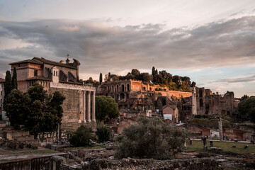 Fototapeta premium Ancient Roman Forum ruins and classical temples bathed in golden sunset light under a dramatic sky in Rome, Italy