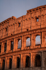 Obraz premium Ancient Colosseum exterior in Rome at golden hour, sunlit stone arches and weathered facade of amphitheater