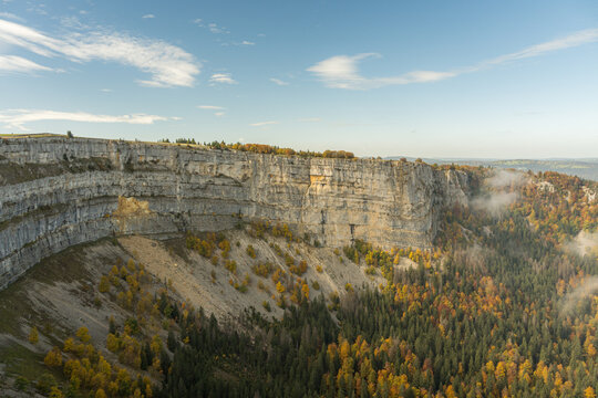 Autumn limestone cliff over forest valley with mist and sky
