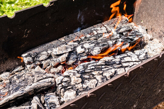 Burning firewood and embers in barbecue grill on summer day