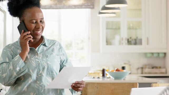 Woman holding phone reading paper in kitchen, dark discs passing, occluding view on finance call