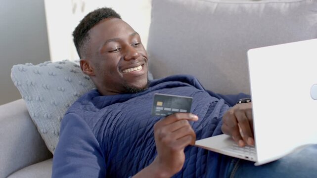 Man reclining on sofa, typing on laptop with card, making online payment and causing coin graphic
