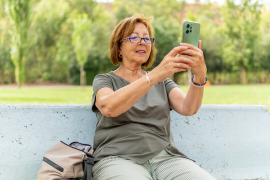 Senior woman taking a selfie on a park bench outdoors