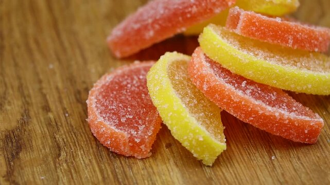 Lemon and orange jelly slices coated in sugar, rotating close-up on a wooden table.