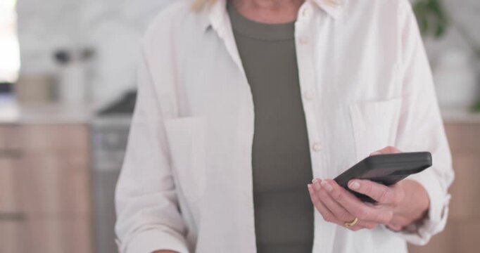Senior woman holding phone, responding to reminder and preparing pills in pill organizer in kitchen