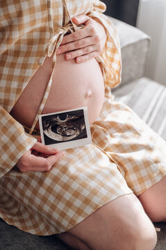 Pregnant woman relaxing on sofa holding ultrasound photo