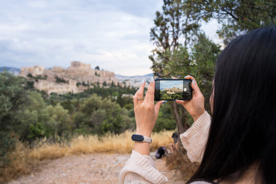 Woman photographing ancient hilltop city with smartphone