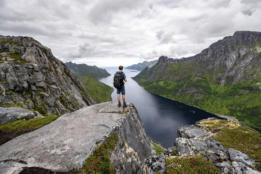 View of &Oslash;yfjorden fjord and mountains, view from Barden mountain, young man standing on a cliff, Senja, Norway